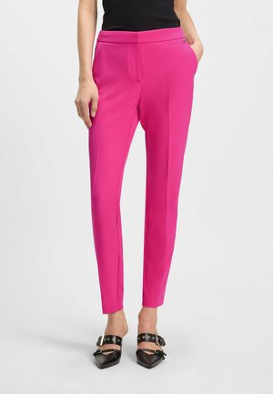 Pantaloni aderenti di un vivace rosa, con una texture liscia e gambe affusolate. Presentano una vita piatta e un dettaglio logo discreto. Abbinati a scarpe nere.