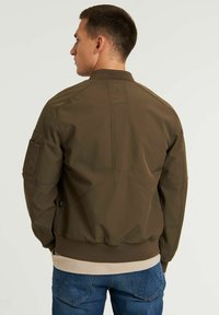 Giacca bomber verde oliva con collo e polsini a coste, tasche laterali e una texture liscia. Dettagli di cucitura notevoli sul retro.