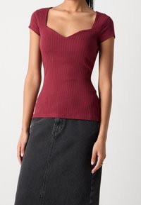Top a coste color marrone con maniche corte e scollo quadrato, abbinato a una gonna di jeans nera. Il tessuto ha una consistenza liscia.