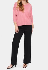 Light pink cardigan with button closure, 3/4 sleeves, and ribbed hem, paired with tailored black pants and strappy black sandals.