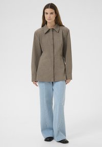 Brun, skræddersyet jakke med lange ærmer og spidse krave, frontknaplukning og strukturerede sømme, parret med lyseblå, bredde jeans.