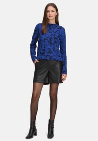 Niebiści sweter z wzorem dzianinowym, z czarnymi akcentami, w połączeniu z czarnymi skórzanymi szortami, przezroczystymi czarnymi rajstopami i czarnymi botkami za kostkę.