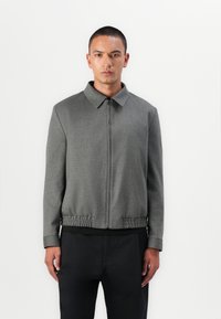 Jachetă gri cu fermoar, cu guler, tiv elastic și mâneci lungi. Textură netedă, design ajustat și stil minimalist.