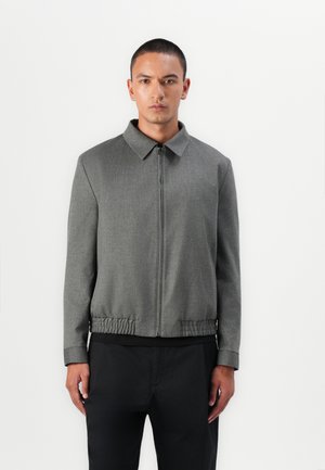 Grey zip-up jacket with a collared neckline, elasticated hem, and long sleeves. Smooth texture, fitted design, and minimalistic style.