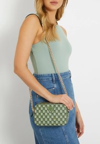 Borsa a tracolla verde a quadri con tracolla a catena dorata e dettaglio del logo; la borsa ha una texture liscia e una forma rettangolare.
