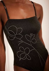 Maillot de bain une pièce noir avec un décolleté carré, ornée de broderies florales métalliques et de bretelles ajustables, texturé avec des accents pailletés.