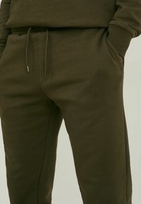 Olivgrüne Sweatpants aus weichem Baumwoll-Mix-Gewebe, mit einem elastischen Bund und verstellbarem Kordelzug sowie seitlichen Taschen.