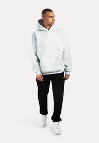 Jasnoszara kieszonkowa bluza z kapturem o luźnym kroju, z białym logo z przodu. Połączona z czarnymi spodniami i białymi trampkami.