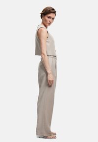 Beige cropped vest top og vide bukser lavet af et let materiale. Outfittet har en bælte i taljen og slanke stropper, med diskrete knapper.