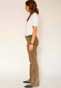 Jean évasé en velours côtelé marron avec poches avant, porté avec un t-shirt blanc et des chaussures noires à bout pointu, accessoirisé d'une écharpe marron.