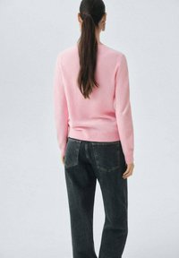 Suéter rosa de un tejido suave y liso con mangas largas, combinado con jeans de mezclilla oscura de corte clásico y bolsillos traseros.