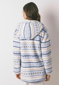 Faux fur hooded jas met horizontale strepen in lichtblauw, marineblauw en crème, versierd met patronen en een zachte textuur.