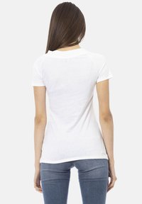 T-shirt bianco a maniche corte con un design aderente, scollo rotondo a coste e texture liscia, abbinato a jeans blu aderenti.