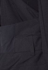 Black fabric overalls featuring a textured surface, multiple pockets, and adjustable straps, designed for functional wear.