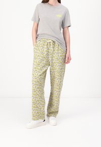 Grå bomullströja med korta ärmar, i kombination med gula och grå mönstrade sweatpants med banandesign. Vita sneakers fulländar looken.