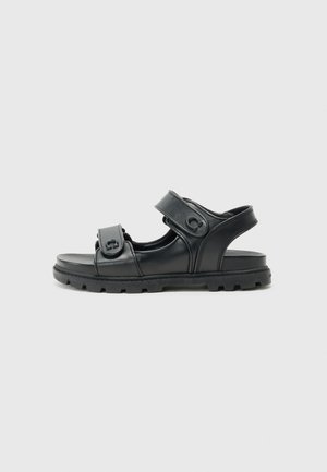 Black sandal made of smooth leather, featuring two adjustable straps and a thick textured sole with grip patterns. Open-back design.