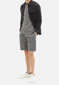 Giacca navy, t-shirt a righe in bianco e nero, pantaloni corti grigi e sneakers bianche. Look casual con tasche sulla giacca e sui pantaloni.