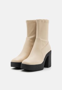 Bottes chevilles en simili cuir beige avec un bout arrondi et un talon plateforme noir texturé, dotées d'une tige ajustée et de détails de couture minimalistes.