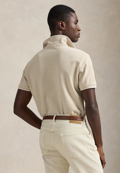 Μπεζ πουκάμισο πόλο με ρίγες και ψηλό γιακά, συνδυασμένο με παντελόνι σε κρεμ απόχρωση και καφέ δερμάτινη ζώνη με ταμπελάκι επώνυμης μάρκας.