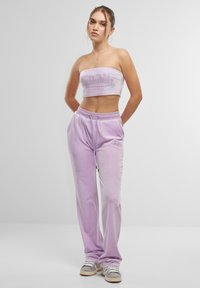 Lila velours crop top met logo detail, gecombineerd met bijpassende joggers met een elastische tailleband en trekkoord. Sneakers met grijze accenten.