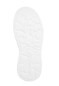 Semelle d'une chaussure blanche avec des motifs de rainures irréguliers, ondulés et incurvés pour une meilleure adhérence sur fond blanc uni.