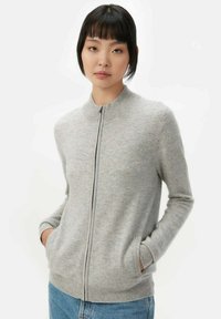 Grå zip-up tröja med rund halsringning, ribbade ärmar och nederkant, tillverkad av ett mjukt, texturerat material. Har sidofickor.