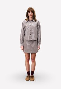 Braun- und cremefarbener Karomuster-Hemd mit passenden Minirock. Getragen mit braunen Schuhen und burgunderfarbenen Socken. Glatter Stoff und taillierte Passform.