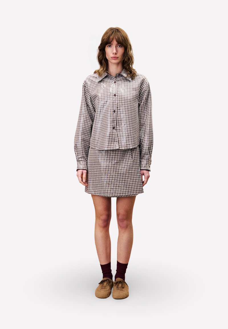 Braun- und cremefarbener Karomuster-Hemd mit passenden Minirock. Getragen mit braunen Schuhen und burgunderfarbenen Socken. Glatter Stoff und taillierte Passform.