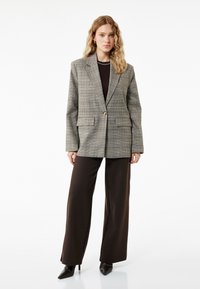Grå ternet blazer med spids krave, enkelt knaplukning og forlommer, parret med brune vide bukser og sorte spidse hæle.