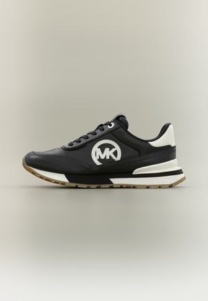 Černobílá teniska Michael Kors z perforované kůže, se šněrováním vpředu a gumovou podrážkou, boční pohled na neutrálním pozadí.