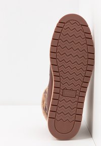Semelle d'une chaussure TOMS marron avec un motif de bande de roulement en zigzag et le nom de la marque centré sur la semelle extérieure en caoutchouc.