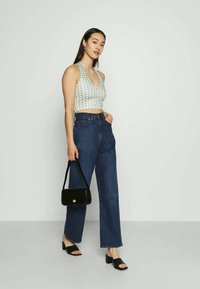 Top cropped em gingham verde-claro com decote halter, combinado com jeans escuros de cintura alta, sandálias pretas tipo slingback e uma pequena bolsa preta.