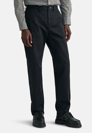 Dunkelblauem Hosen aus gewebtem Stoff mit einem geraden Bein Design, Gürtelschlaufen und einem Reißverschluss. Dazu schwarze Schnürschuhe.