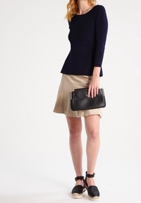 Haut côtelé à manches longues bleu marine associé à une jupe évasée couleur beige. Sac à main noir avec ferrures argentées et espadrilles noires à brides à la cheville.