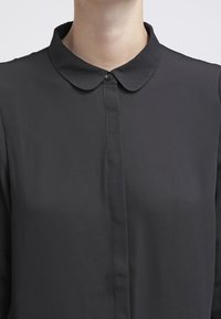Blusa nera con colletto realizzata in un tessuto liscio e leggero. Presenta una chiusura con bottoni sul davanti e dettagli di cucitura discreti.