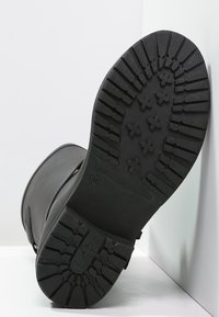 Black rubber boot sole featuring deep treads and cross patterns, designed for traction. Material appears durable with a smooth finish.