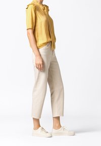 Blusa gialla a maniche corte con motivo testurizzato e scollo arricciato. Abbinata a pantaloni cropped beige chiaro e sneakers bianco sporco con lacci.