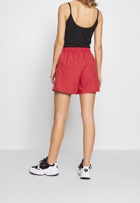 Red athletic shorts with an elastic waistband, side stripes, and a lightweight texture. Worn with a black tank top and white sneakers.