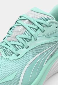 Baskets de sport bleu-vert clair avec dessus en mesh, lacets plats et accents texturés. Présente des lignes blanches lisses et courbes sur le côté.