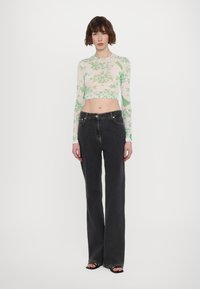 Gjennomsiktig langermet topp med grønt blomstermønster; kombinert med høy midje, vide svarte jeans; modellen står frontvendt.