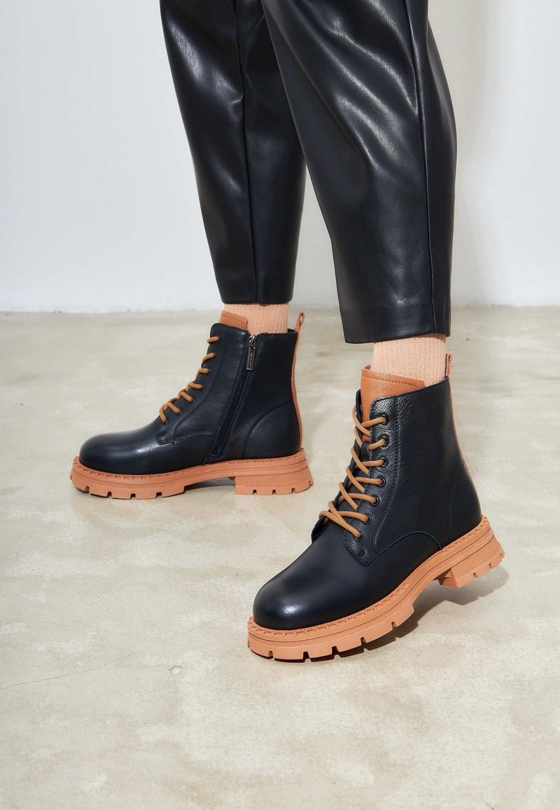 Bottes cheville en cuir noir avec semelles en caoutchouc beige et lacets. Dotées d'une fermeture éclair latérale pour un enfilage facile et de coutures décoratives sur la semelle.