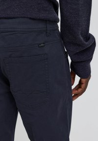 Navy blue cotton trousers featuring a back pocket with subtle stitching details, part of a casual outfit with a dark sweater visible.