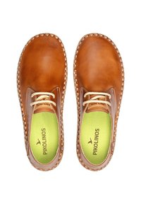 Zapatos de cuero color tostado con forma redondeada, con un borde trenzado, cordones beige y una plantilla interior verde brillante en contraste con el logo de la marca.