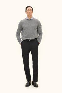 Grauer Wollpullover über einem blau-weiß gestreiften Hemd, kombiniert mit schwarzen, maßgeschneiderten Hosen und schwarzen Lederschuhen, vor einem hellen Hintergrund stehend.