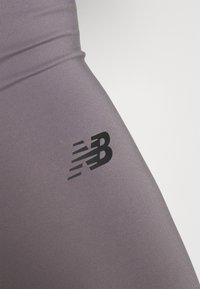 Fioletowe legginsy o gładkiej, elastycznej fakturze z czarnym logo New Balance z boku.