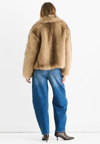 Brown faux fur jacket with a high collar, oversized fit, and long sleeves, paired with loose blue denim jeans and pointy ankle boots.