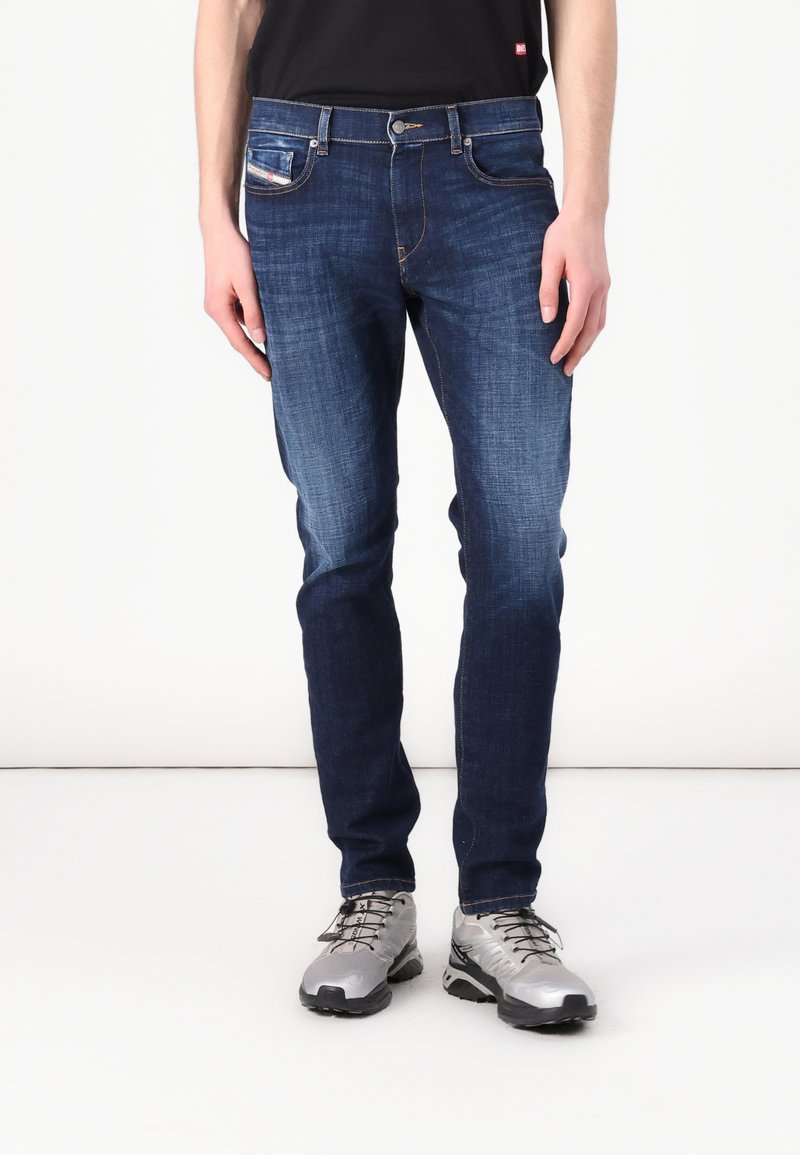 Sötétkék farmernadrág, slim fit szabással, ellentétes varrással, öt zsebbel és klasszikus gombos záródással.