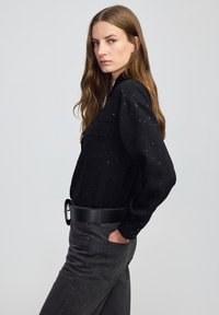 Czarna prążkowana koszula z srebrnym wzorem w kropki, z kieszonką na piersi i mankietami na guziki, zestawiona z ciemnoszarymi spodniami z wysokim stanem i czarnym paskiem.