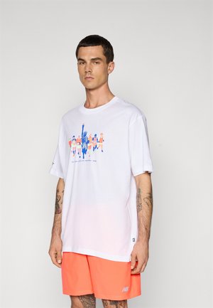 Homme portant un t-shirt blanc avec un graphique de coureurs de marathon colorés et de la Statue de la Liberté, associé à un short orange vif.