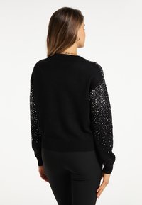 Maglione nero con scollo rotondo, caratterizzato da paillettes nere testurizzate sulle maniche, progettato per un look aderente. Tessuto a maglia morbido.